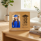 Graduation-themed photo frame on a wooden table with a plant and books in the background