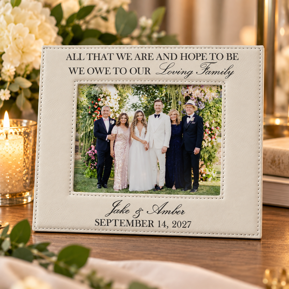 White leatherette wedding frame engraved All That We Are and Hope to Be We Owe to Our Loving Family on a table with candles and flowers