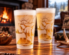 Two Elk Mountain pint glasses with 360° frosted elk and mountain scene, filled with beer in a cabin by the fireplace